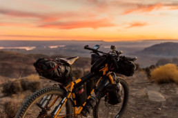A loaded touring bicycle sitting at the top of a cliff with the sunset in the background