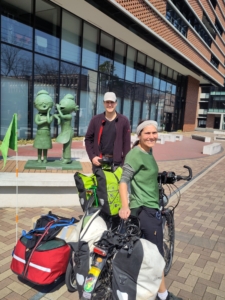 man and woman posing with their bicycles in front of a statue 
